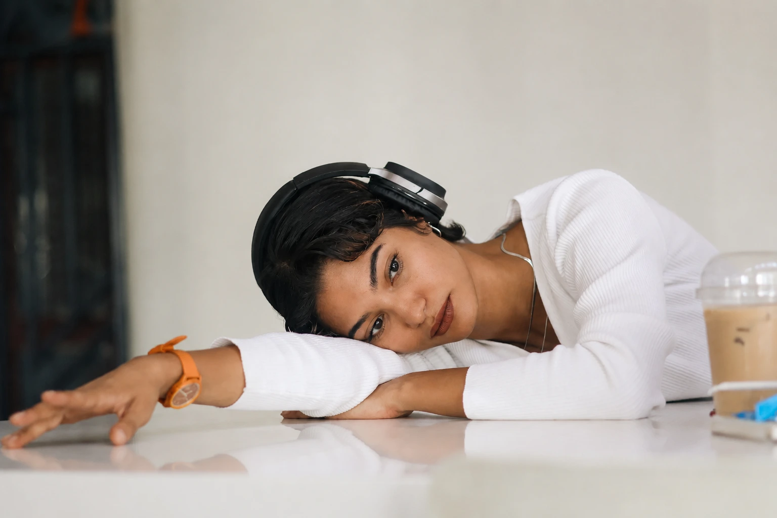 wanita dengan headphone sedang menyenderkan kepala ke tangan kanan yang ada di meja