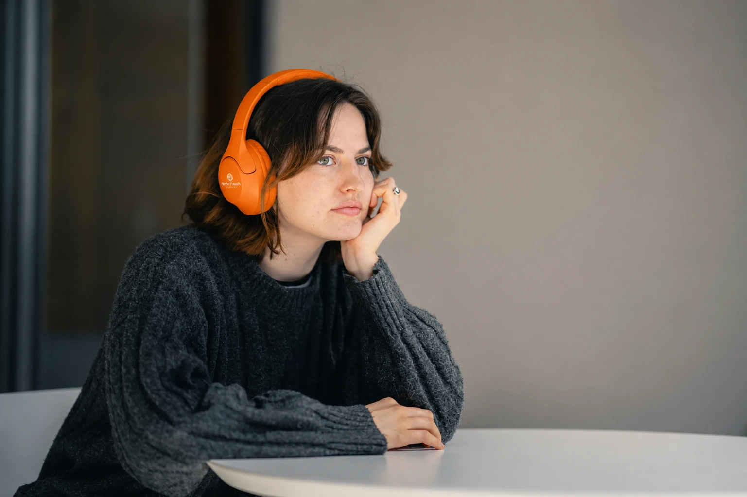 wanita ber headphone orange menopang kepala ke tangan kiri